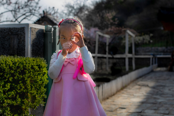Jung Pyong Ri, Nordkorea 2019. Shin Mi-Ryong leker utanför hus nummer 8 där hennes familj bor. De är en av nitton utvalda familjer som tar emot utländska turister i en by för att marknadsföra landets kultur.
