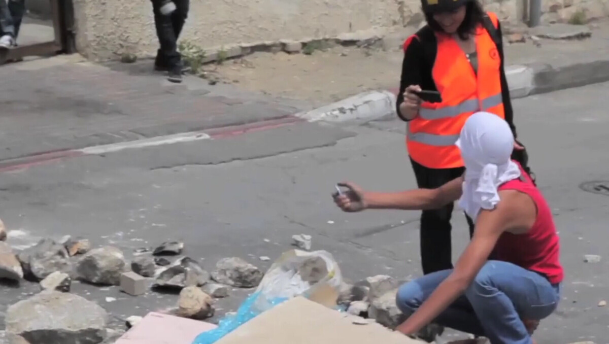 En till synes glad fotograf med mobiltelefon filmar eller fotograferar när en maskerad person är på väg att starta en eld på gatan.