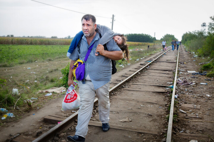 Ungern, september 2015. Muhammed Khalil Ihsain från Homs i Syrien bär sin förlamade dotter Line, 6 år, på sin rygg. Han har 50 meter kvar till gränsen mot Ungern. Så snart han kommer fram dit lämnar han över sin dotter till en volontär och springer tillbaka längs rälsen för att leta efter sin fru. Nu är det knappt en timme kvar tills det att gränsen stängs. Foto: Lotta Härdelin